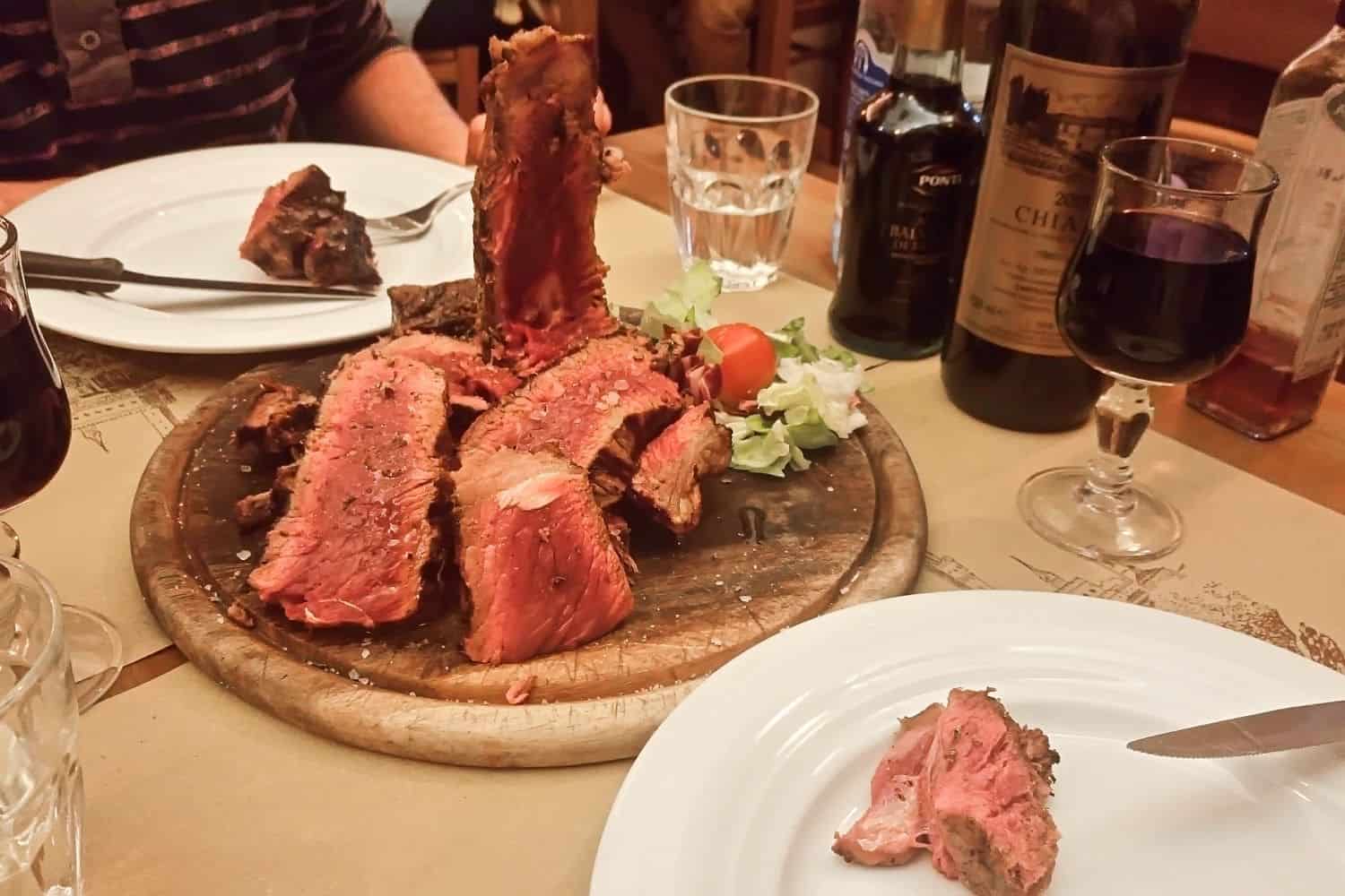 bistecca alla fiorentina in florence - steak with a bit of juices visible and wine glasses on the side