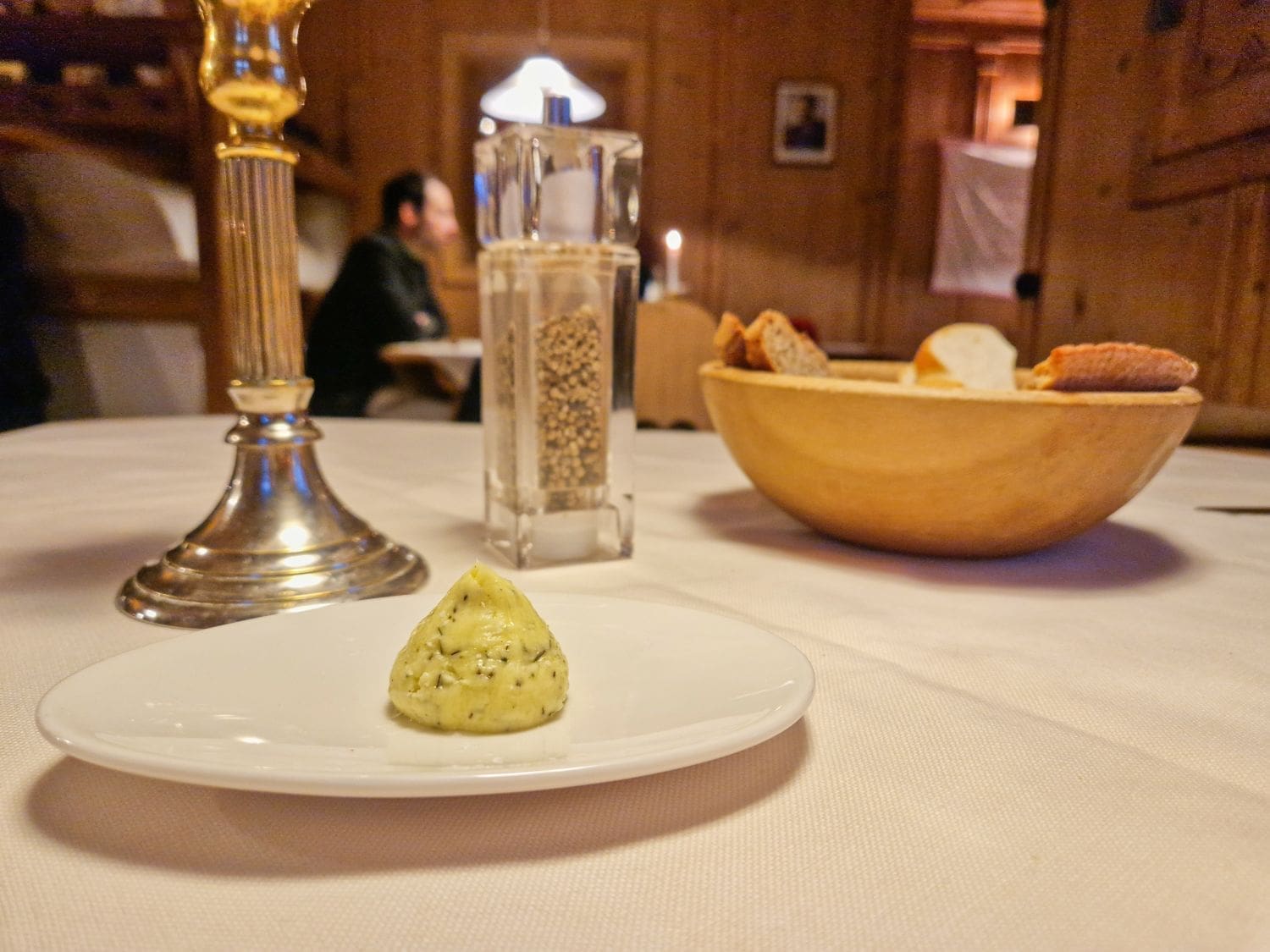 a piece of butter with herbs on a white place and a bread basket on a table in a restaurant in dobbiaco