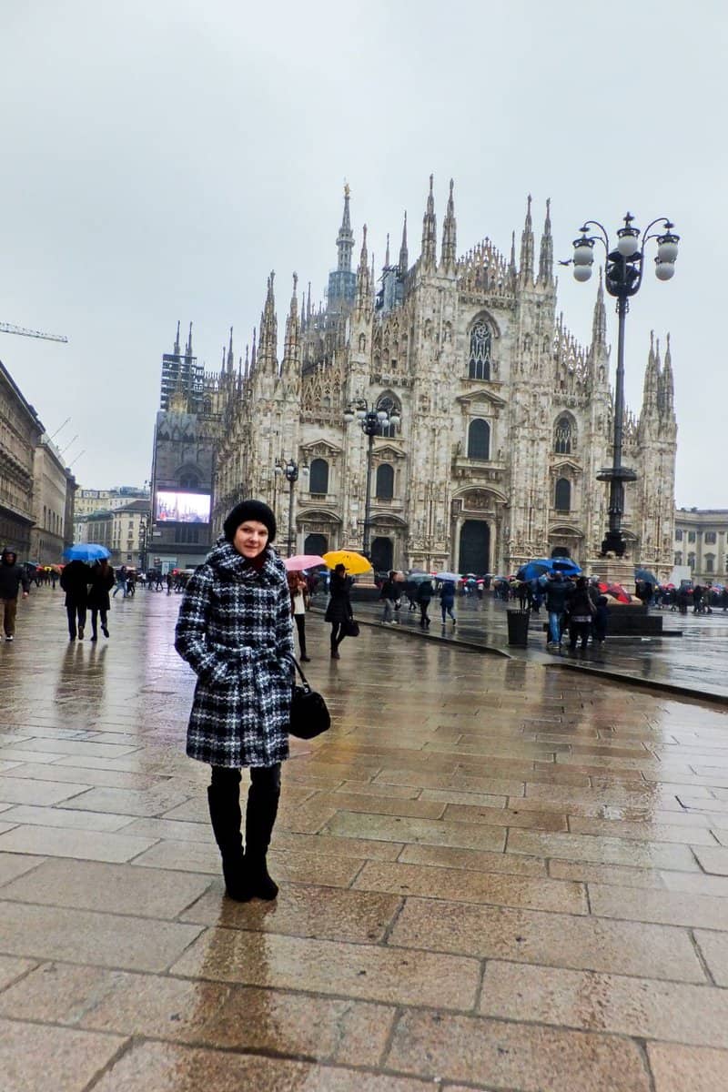 Kristine standing on the piazza del duomo in Milan on a rainy morning, lots of people with umbrellas in the background