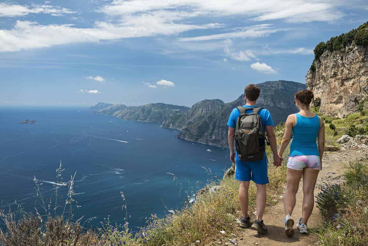 hiking sentiero degli dei in italy - a couple holding hands on the trail with the blue Mediterranean sea visible in the background