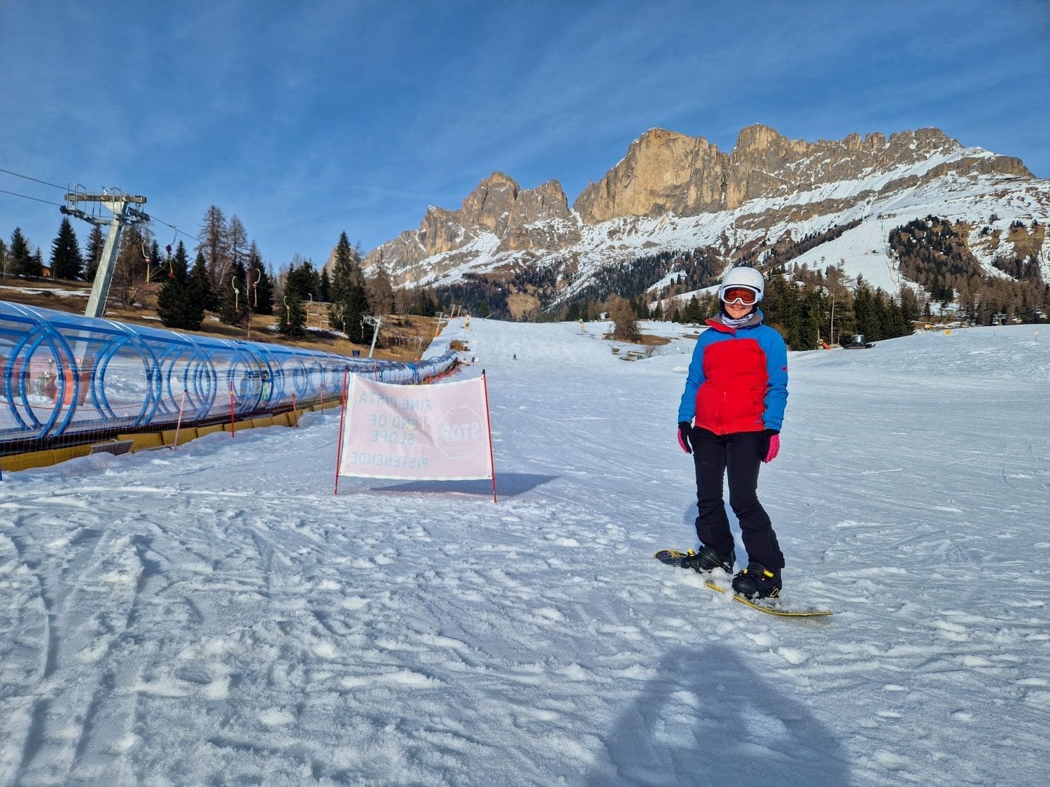 kristine on snowboard in carezza in the dolomites with sun-covered mountains in the background