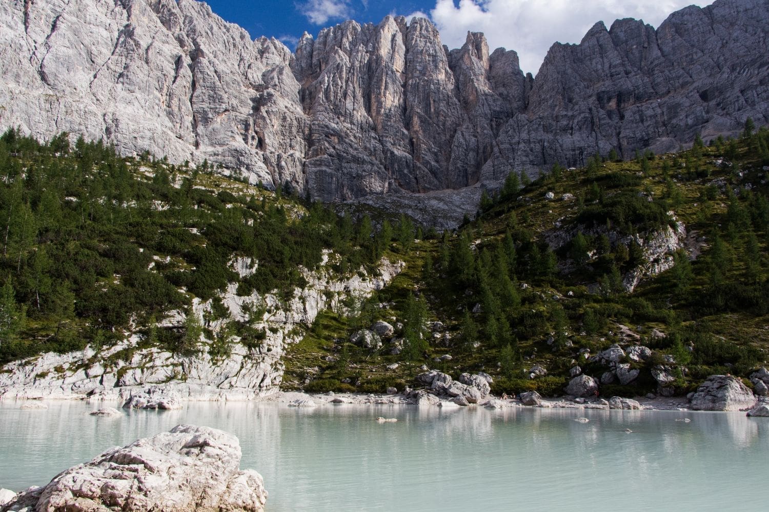 lake sorapis with a milky green water, trees above it, and mountains in the background