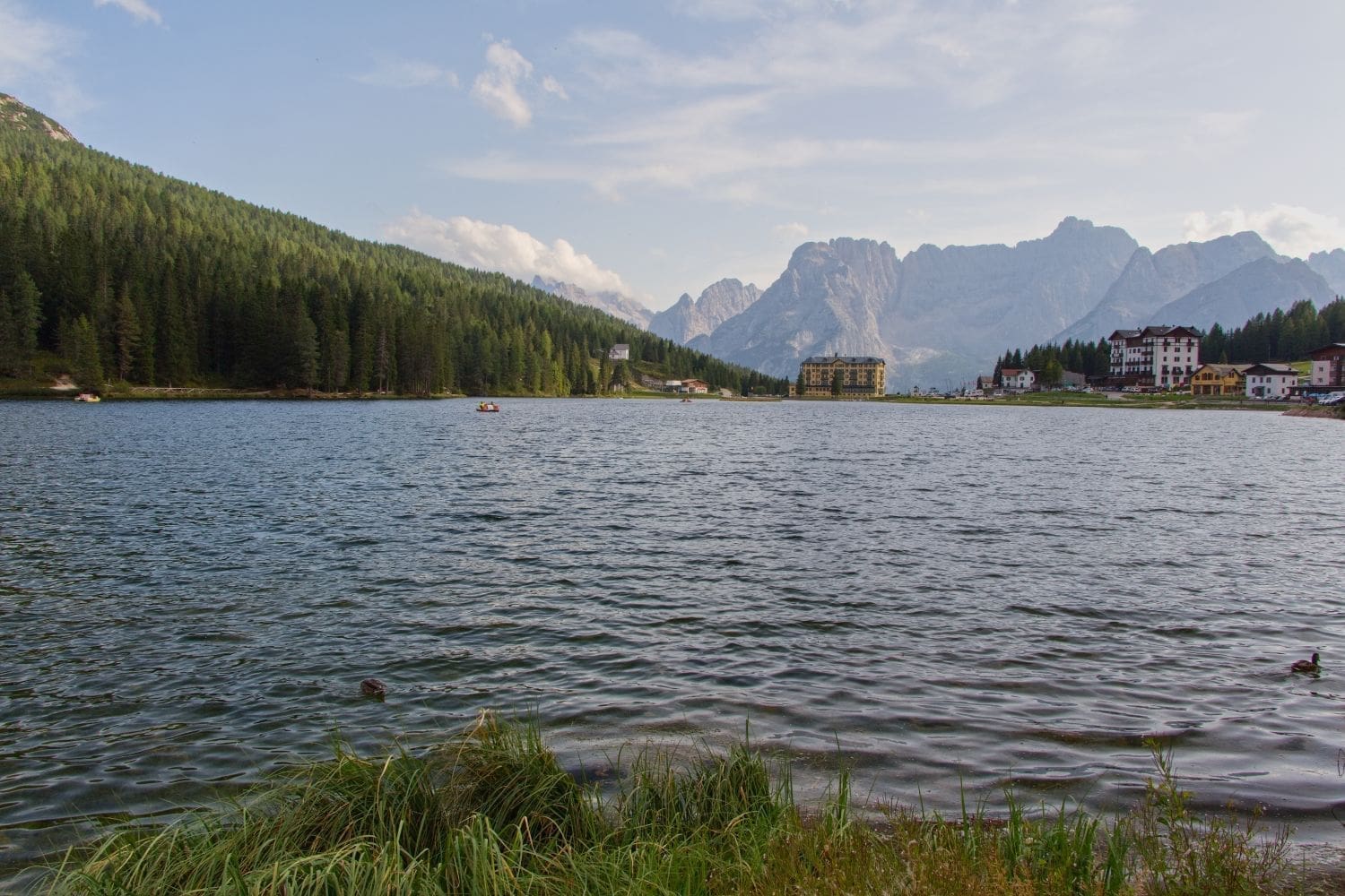 view of lake misurina with some buildings on the far coast and mountains in the background