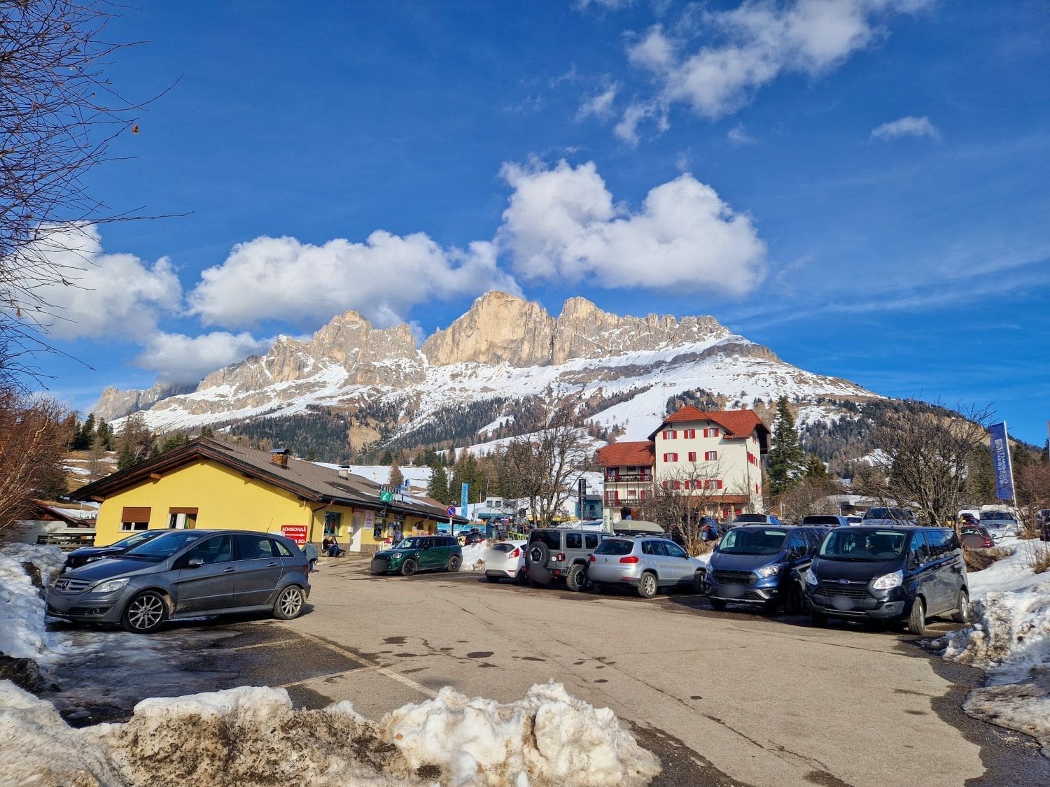 a parking lot next to a ski school full of cars with high mountains in the background