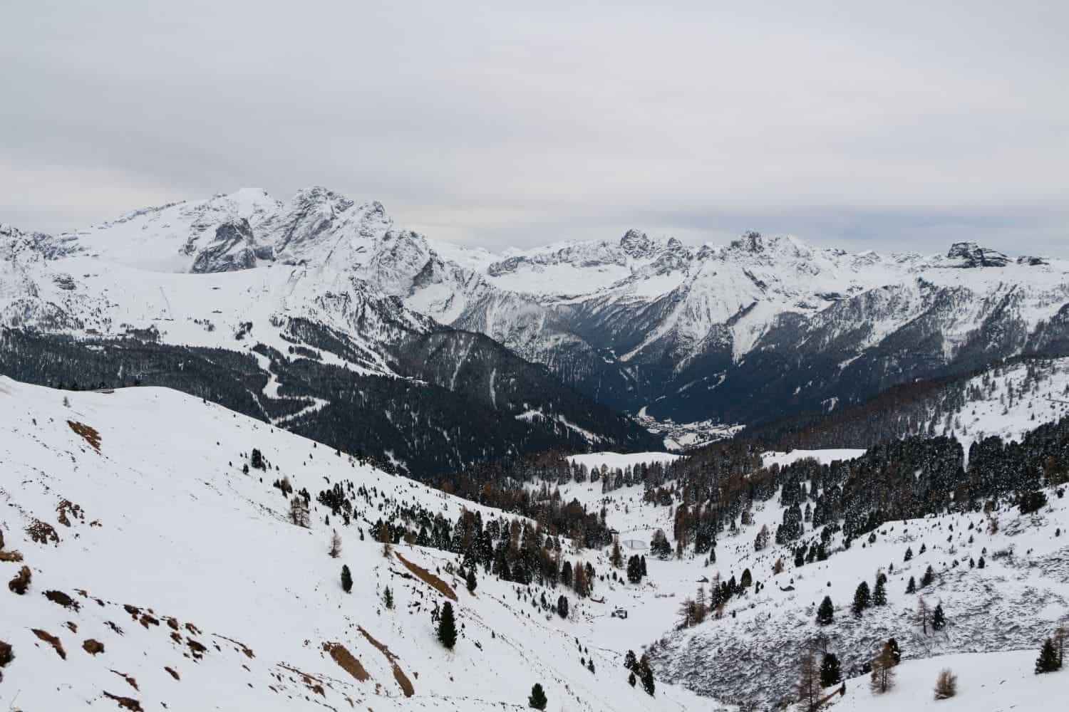 passo sella in the dolomites with big snowy mountains, snowy hills, and trees