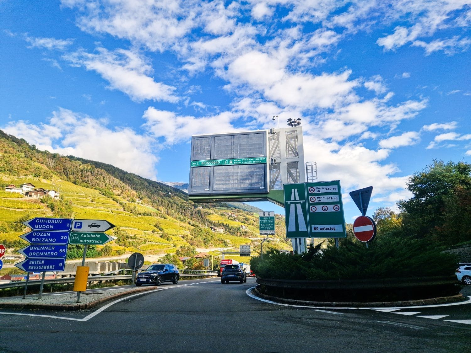 entrance to a toll road in italy autostrada brennero from a roundabout with signs pointing to different towns and a highway sign