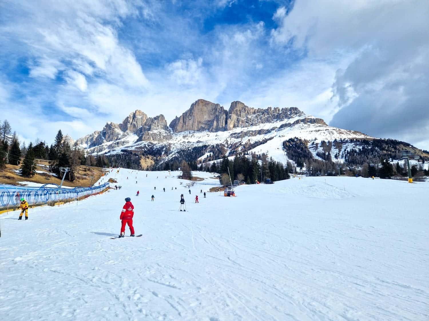 lots of skiers on a slope in the carezza dolomites with snowy mountains in the background