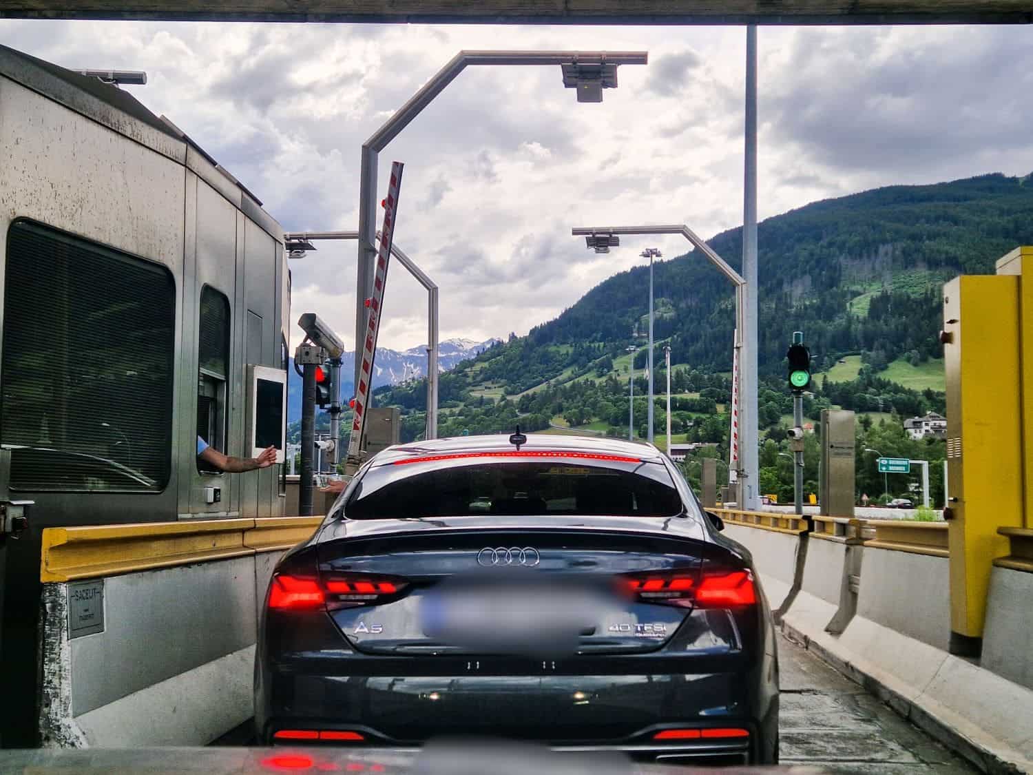 a manned exit booth at the autostrada in the dolomites with a black audi passing through an open barrier