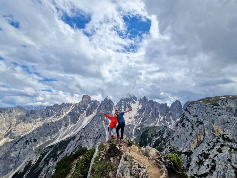 michal and kristine with their arms stretched with the cadini di misurina spiky mountains in the background