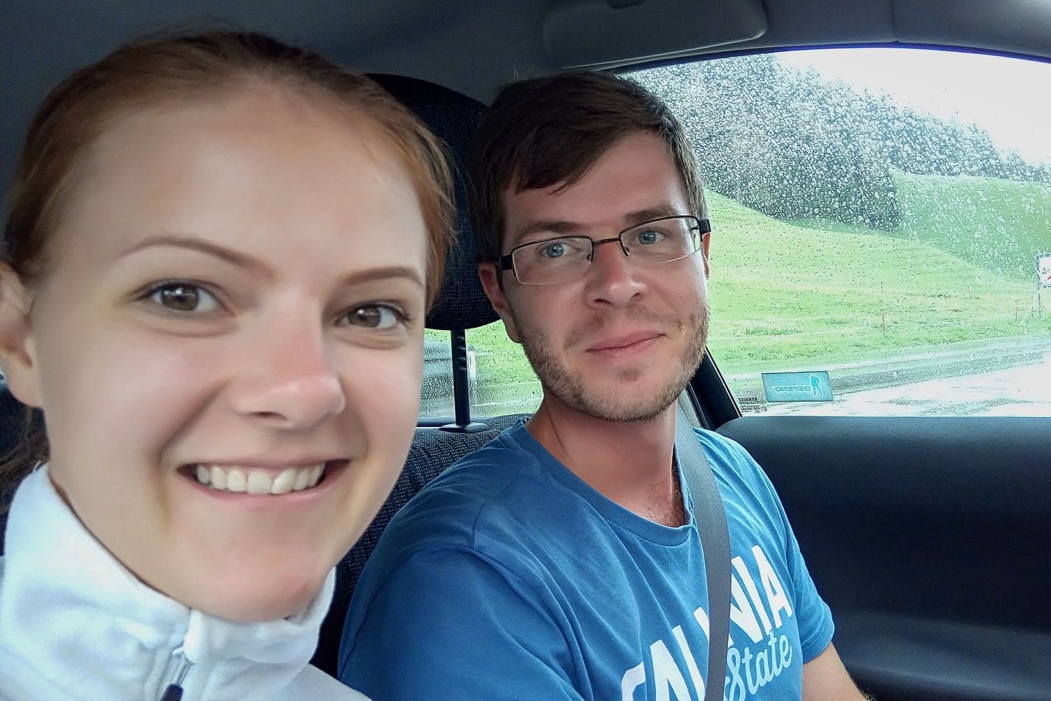 selfie of a smiling Kristine and Michal sitting in a car with raindrops on the window