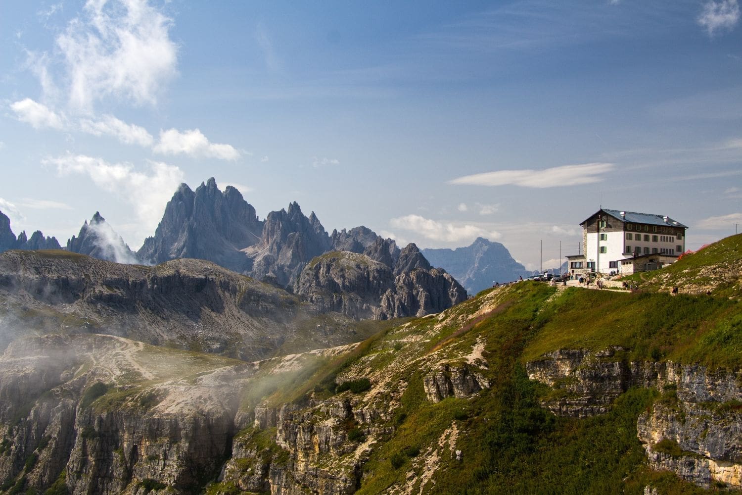 view from tre cime hike in the dolomites in summer with peaks of misurina in the clouds and rifugio alfonso on the right side