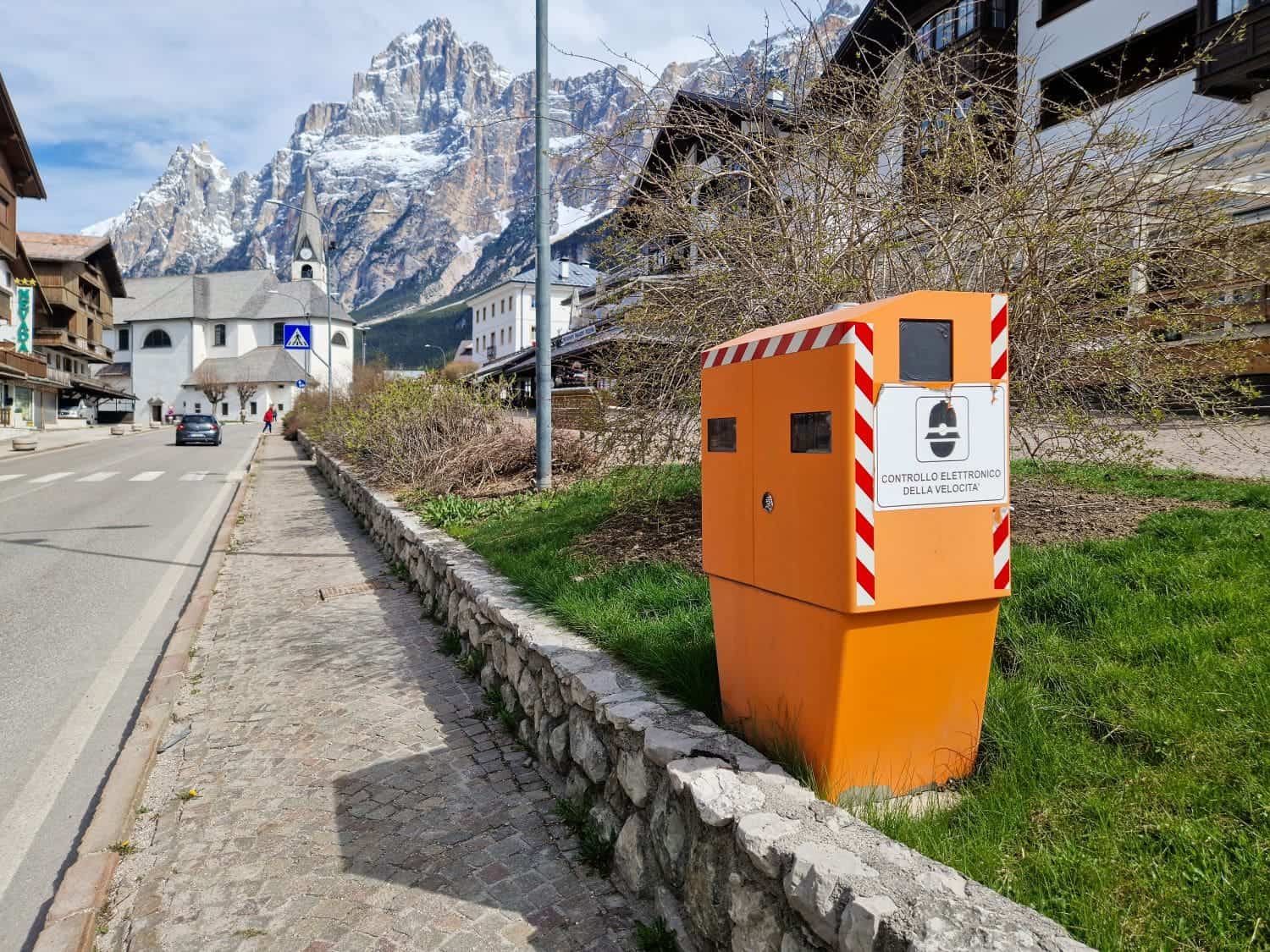 an orange speed camera on a road in a village in the dolomites