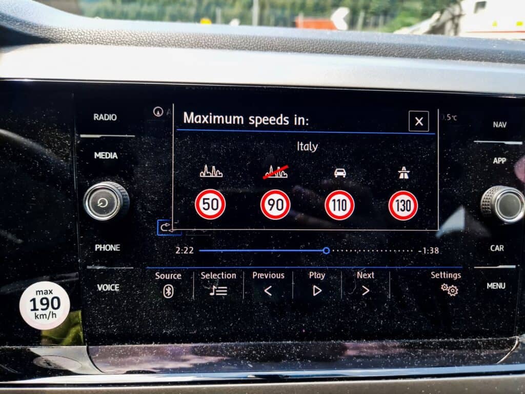 A car's infotainment screen displays maximum speed limits for Italy: 50 km/h in urban areas, 90 km/h on secondary roads, 110 km/h on main roads, and 130 km/h on motorways. A speedometer sticker shows a max speed of 190 km/h.