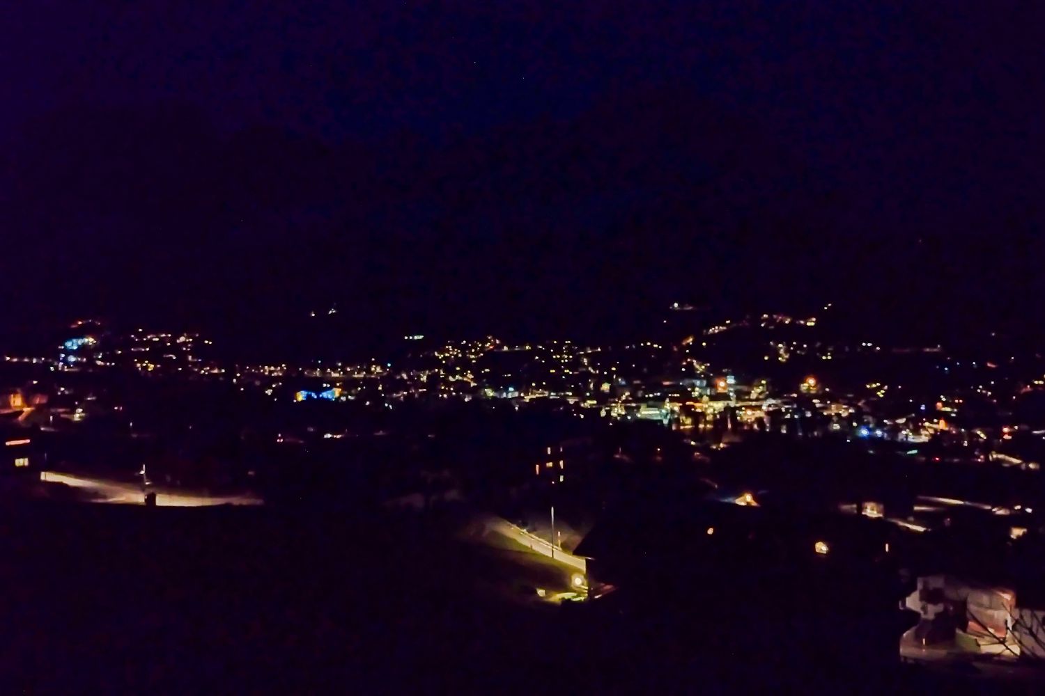A night view of a town with scattered streetlights and building lights glowing in the darkness; the surrounding area is mostly dark, highlighting the illuminated town center.