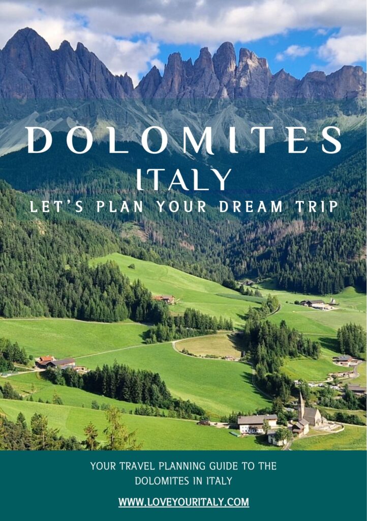 Scenic promotional graphic that reads Dolomites Italy Let’s plan your dream trip over a sweeping view of rolling green meadows, scattered farmhouses, and a small church beneath the jagged Dolomites peaks and a partly cloudy blue sky. A banner at the bottom says Your travel planning guide to the Dolomites in Italy and www dot loveyouritaly dot com.